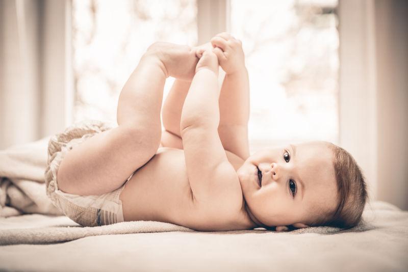 躺在床上抱着自己的小脚丫玩耍的可爱的小婴儿