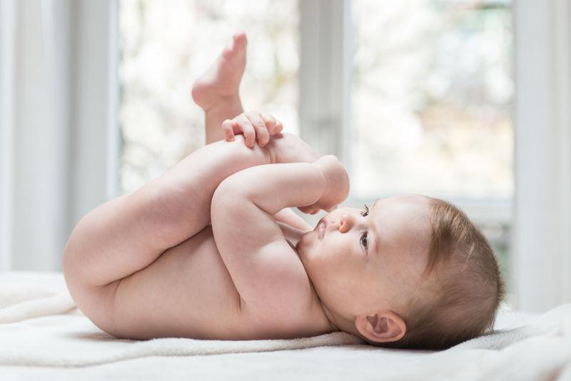 躺在床上抱着腿的快乐的小婴儿