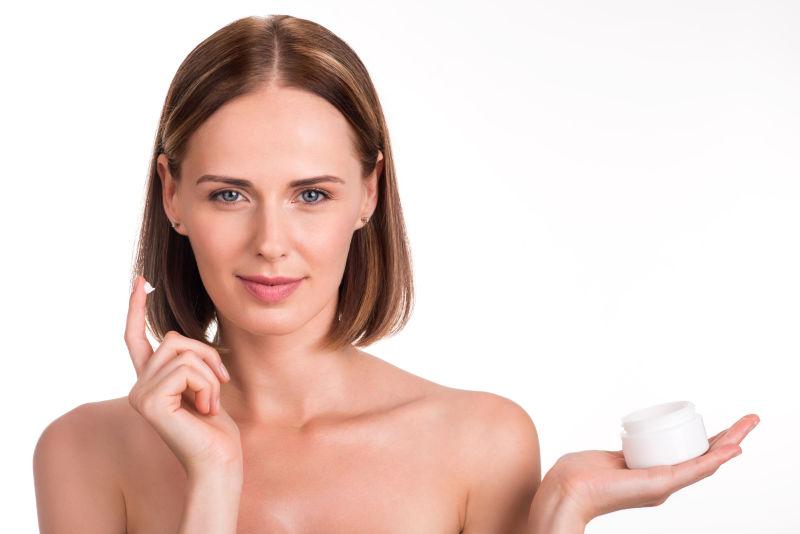 白色背景下年轻积极乐观的女人在隔离的白色背景上使用保湿霜