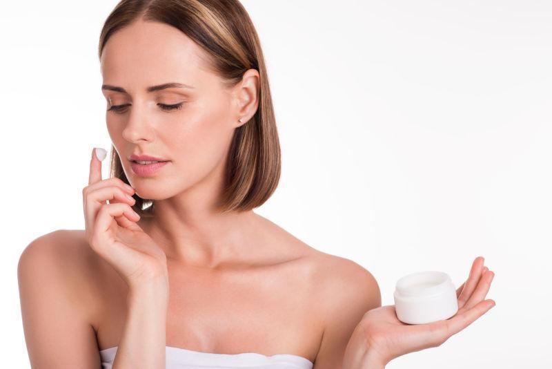 年轻快乐的女人在白色的背景上涂抹保湿霜