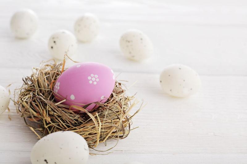 白色桌上的白色鸡蛋和草窝里的粉色复活节彩蛋