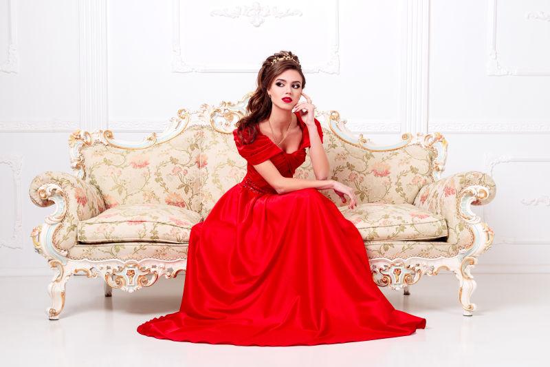 白色背景中坐在沙发上穿红色长裙的气质美女