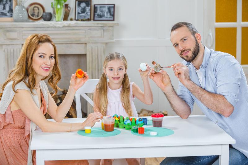快乐的年轻家庭坐在桌子上画复活节彩蛋