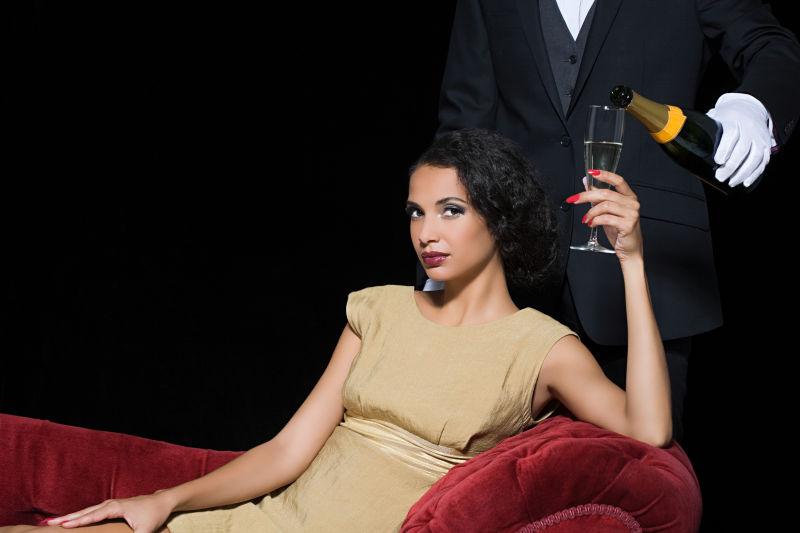 男仆给沙发上的美女倒香槟酒
