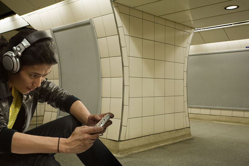 男人坐在地铁戴耳机玩游戏