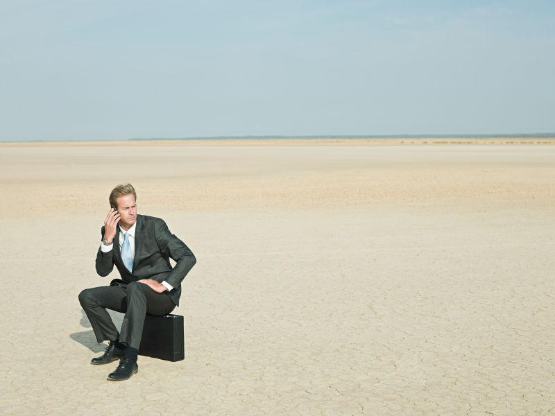 商人坐在干旱土地的公文包上打电话