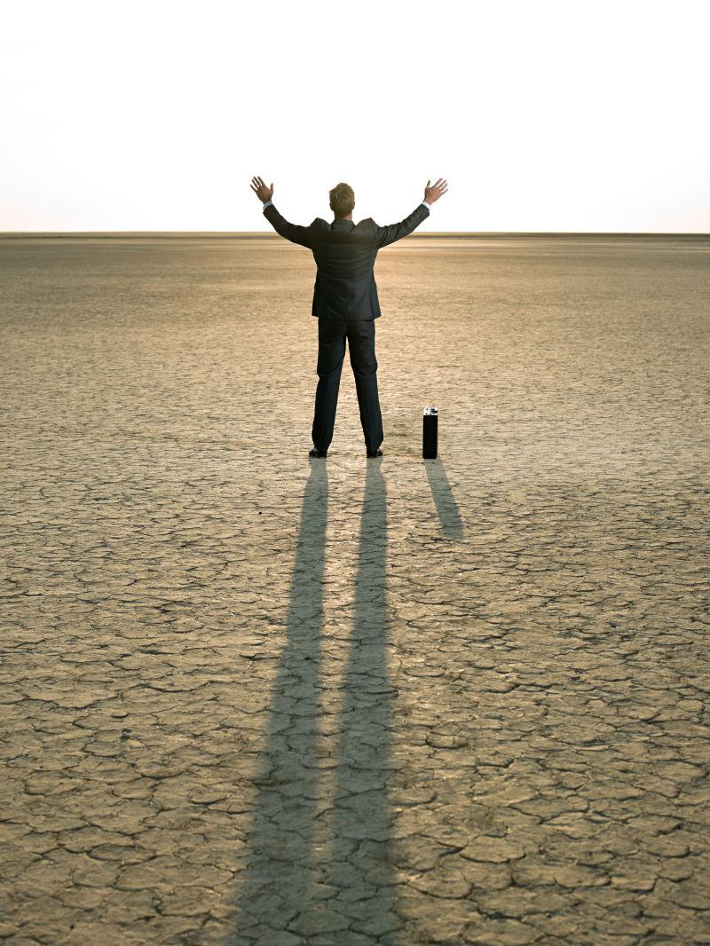 干旱土地上张开双臂走向阳光的商人