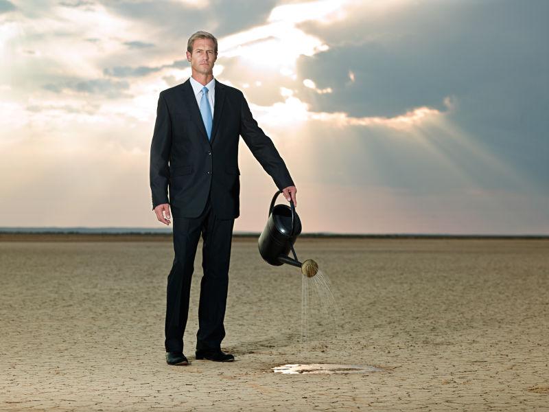 干旱土地上用喷壶往地上浇水的商人