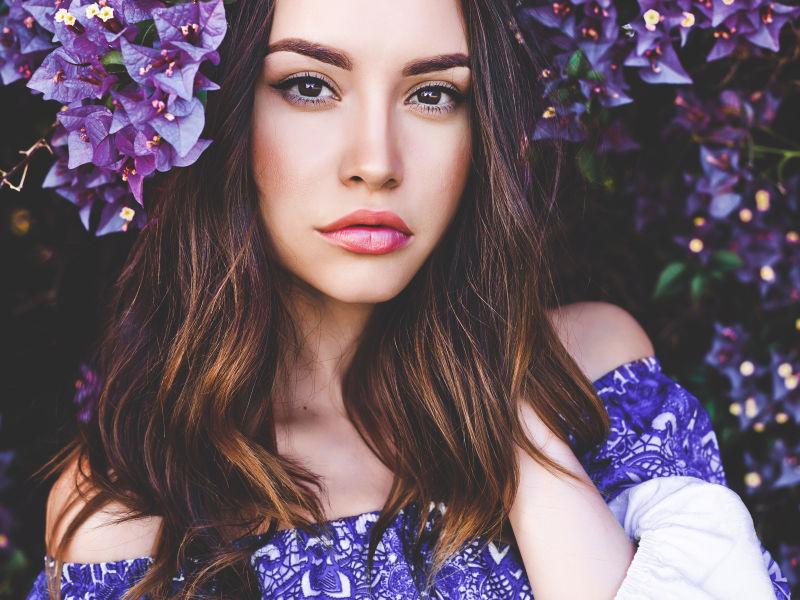 躲在紫色的花朵中间的手抚摸头发的美女