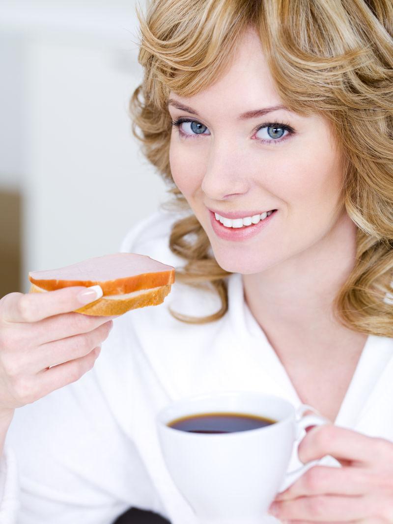 快乐微笑的美丽女人喝着咖啡吃三明治