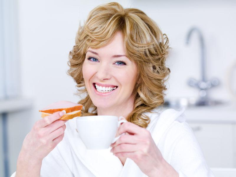 微笑的年轻漂亮的女人在早餐时喝咖啡