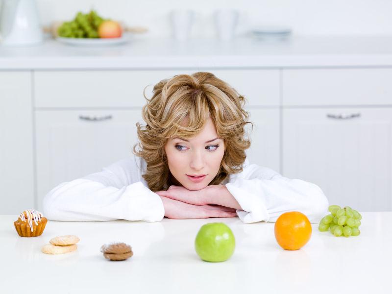 美丽的年轻女子坐在厨房里选择健康的水果和美味的蛋糕