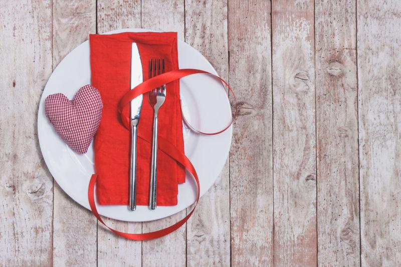 木板上白色盘子里的刀叉彩带和针织心