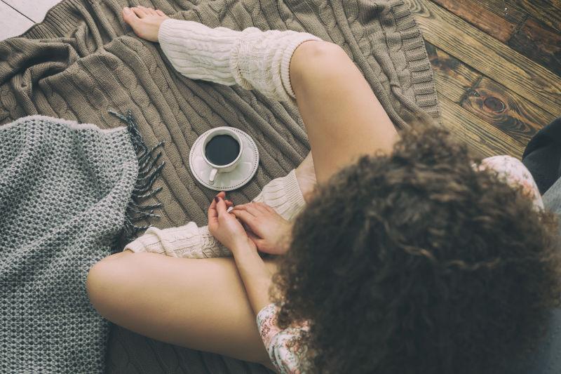 年轻的高加索女孩坐在床旁的地板上身着浴衣和暖袜子