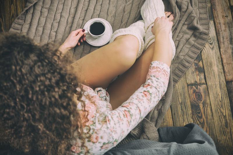 俯视年轻的高加索女孩坐在床旁的地板上喝咖啡