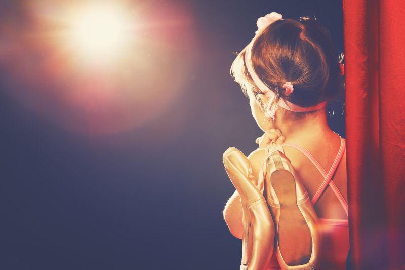 聚光灯下拿着舞蹈鞋的小女孩