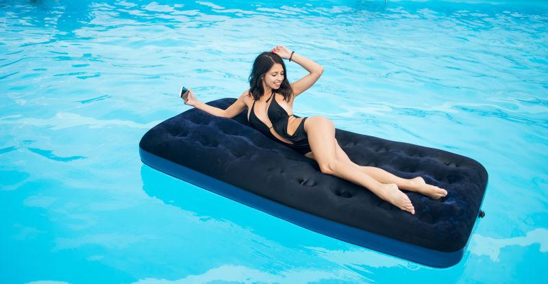 穿着泳装的黑比基尼女人躺在游泳池里的床垫上