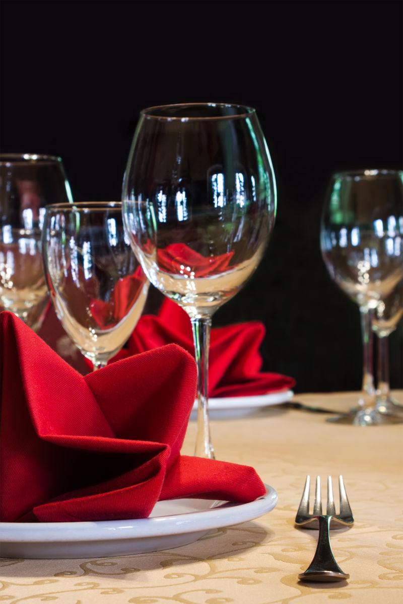 黑色背景中的配有叉子和酒杯的白盘子和红餐巾