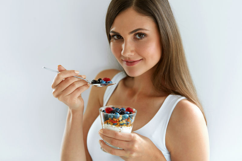 灰色背景上拿着浆果酸奶的美女