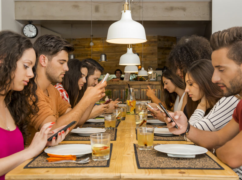 聚会上一群人坐在餐桌边玩手机