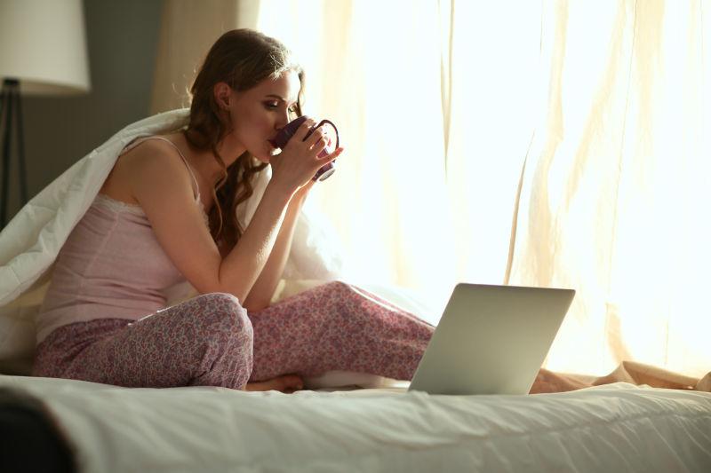 漂亮的女人坐在床上看笔记本