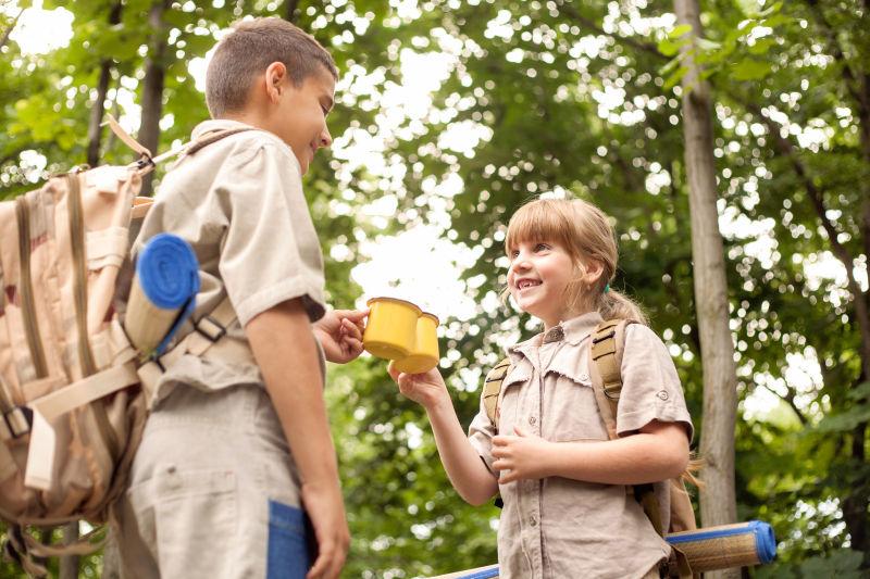 绿色树木背景下的露营中的男孩和女孩干杯