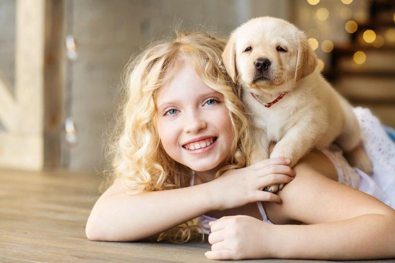 趴在木桌上背着拉布拉多小狗的小女孩