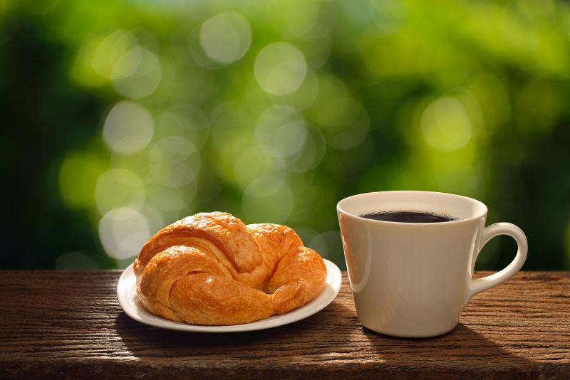 绿色背景下的木桌上的羊角面包和一杯热咖啡