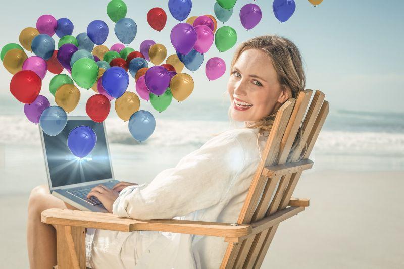 坐在海滩上使用笔记本电脑的微笑的美女