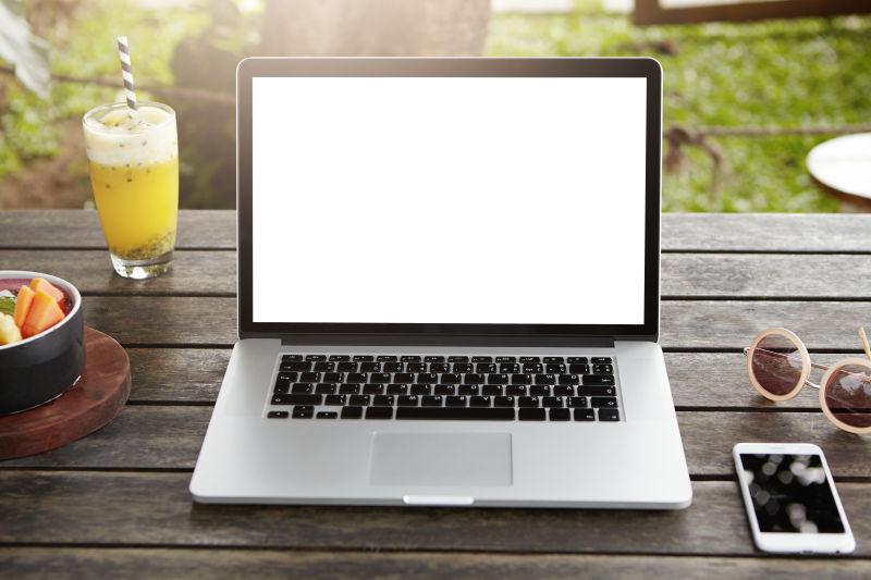 时尚女性的笔记本电脑和手机食品太阳镜一起放在木桌上