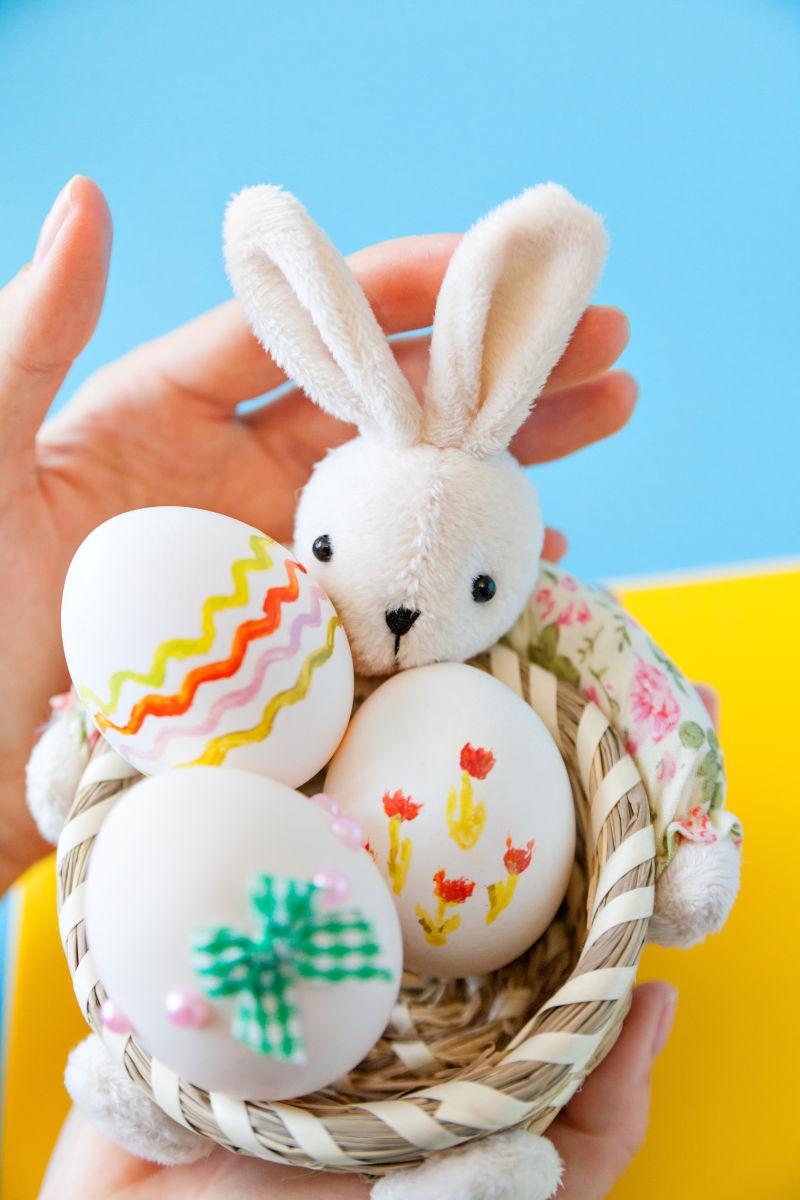 手里拿着一个小篮子里面有可爱的兔子和复活节彩蛋