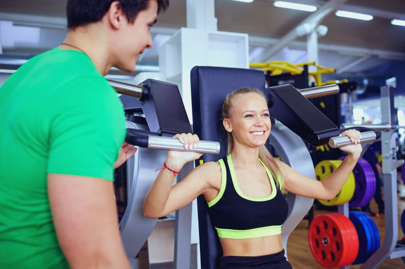 在健身教练的指导下练习举重健身的美女