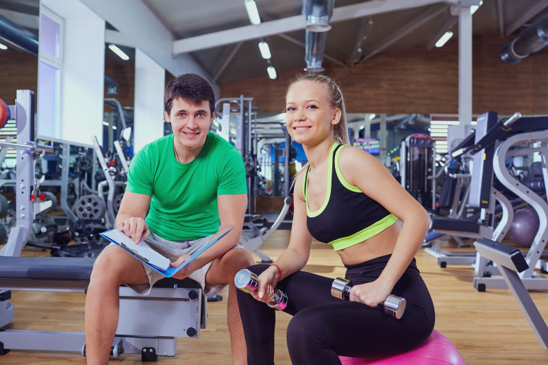 在健身教练的指导下放松做哑铃的美女