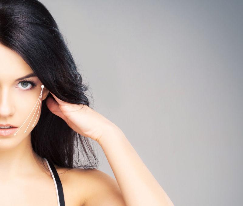 灰色背景上一个脸上画有白色箭头的黑发美女