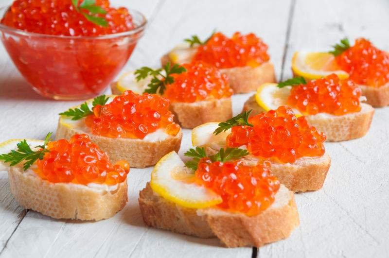 白色木板上的一碗鱼子酱和柠檬鱼子酱面包