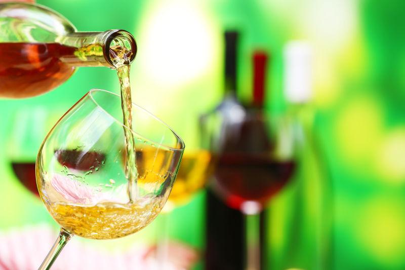 绿色背景下向高脚杯中倒入葡萄酒
