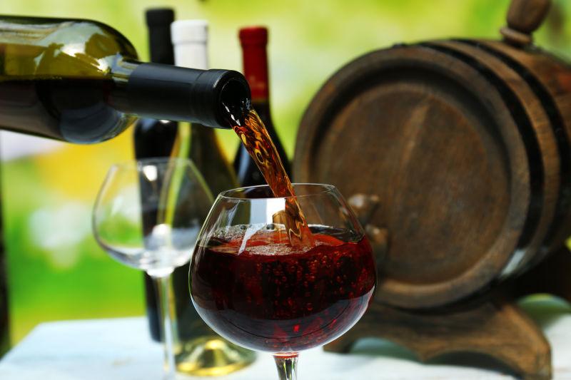 木酒桶和酒瓶背景下向高脚杯中注入红酒