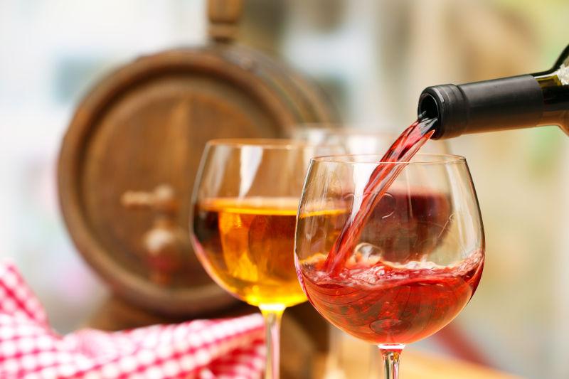 木酒桶和红色桌布背景下向高脚杯中注入红酒