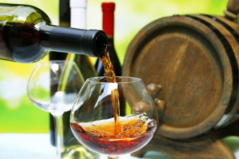 木酒桶和酒瓶背景下向高脚杯中倒入红酒