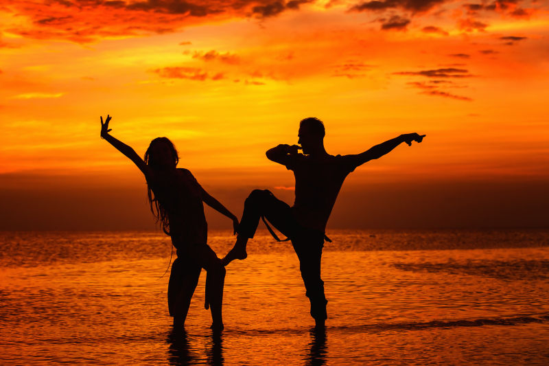 黄昏时站在海滩上摆姿势的年轻夫妻剪影