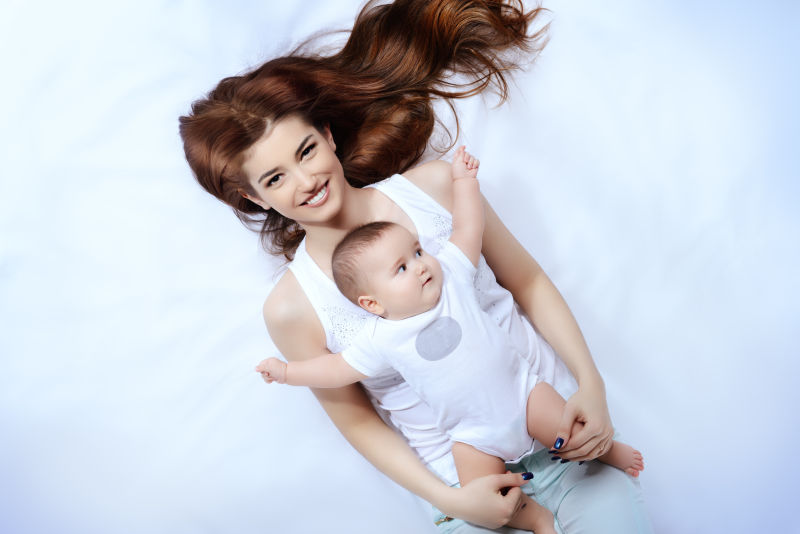 美丽母亲和躺在身上的可爱的婴儿