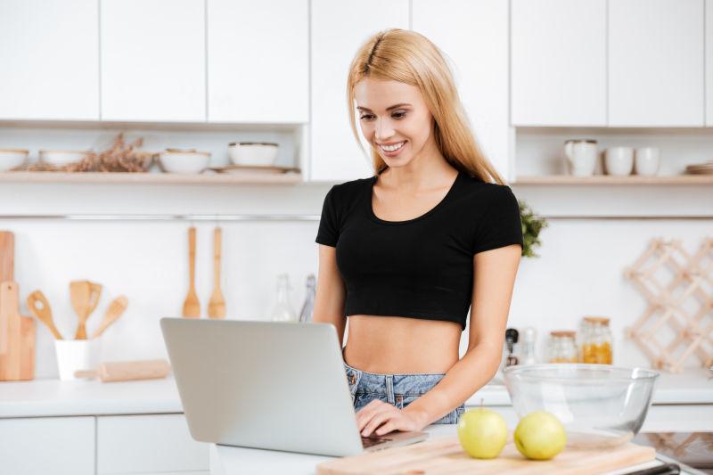 微笑的女人在厨房里使用笔记本电脑