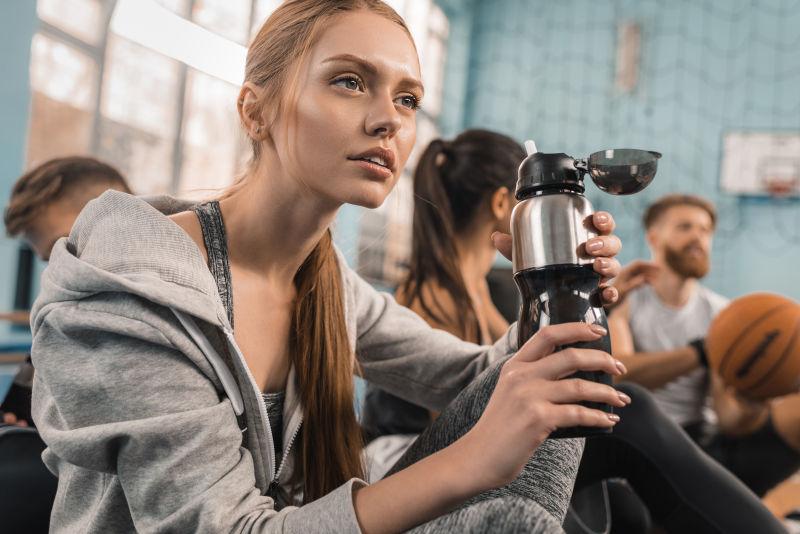 年轻运动员坐在体育馆里拿着运动瓶