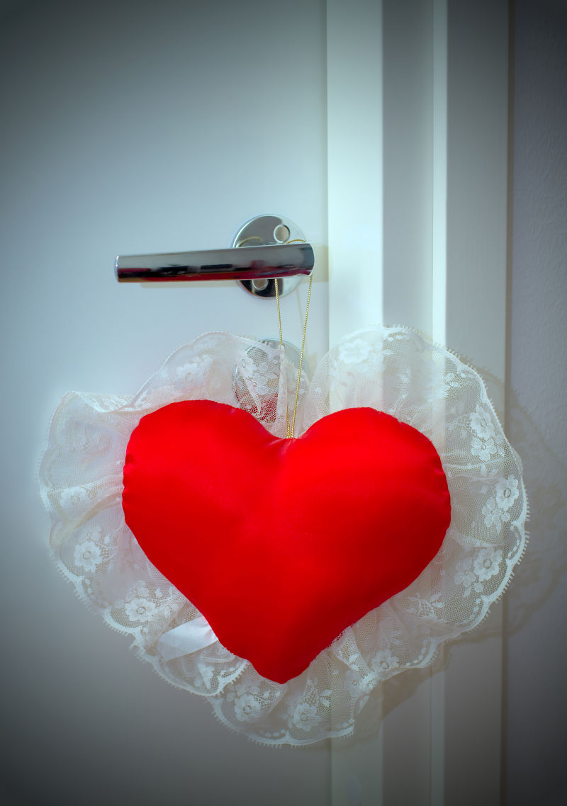 白色背景中挂在门把手上的红色心形抱枕