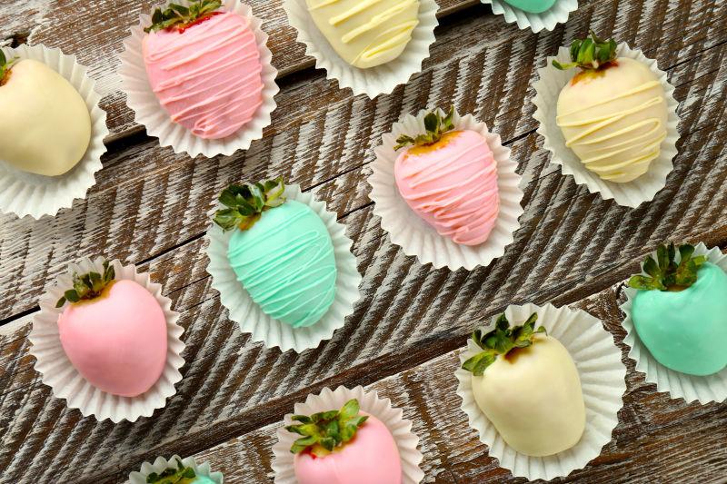 木制背景下草莓上覆盖着丰富多彩的巧克力糖衣