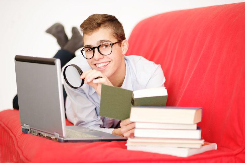 趴在沙发上的男孩拿着放大镜看书