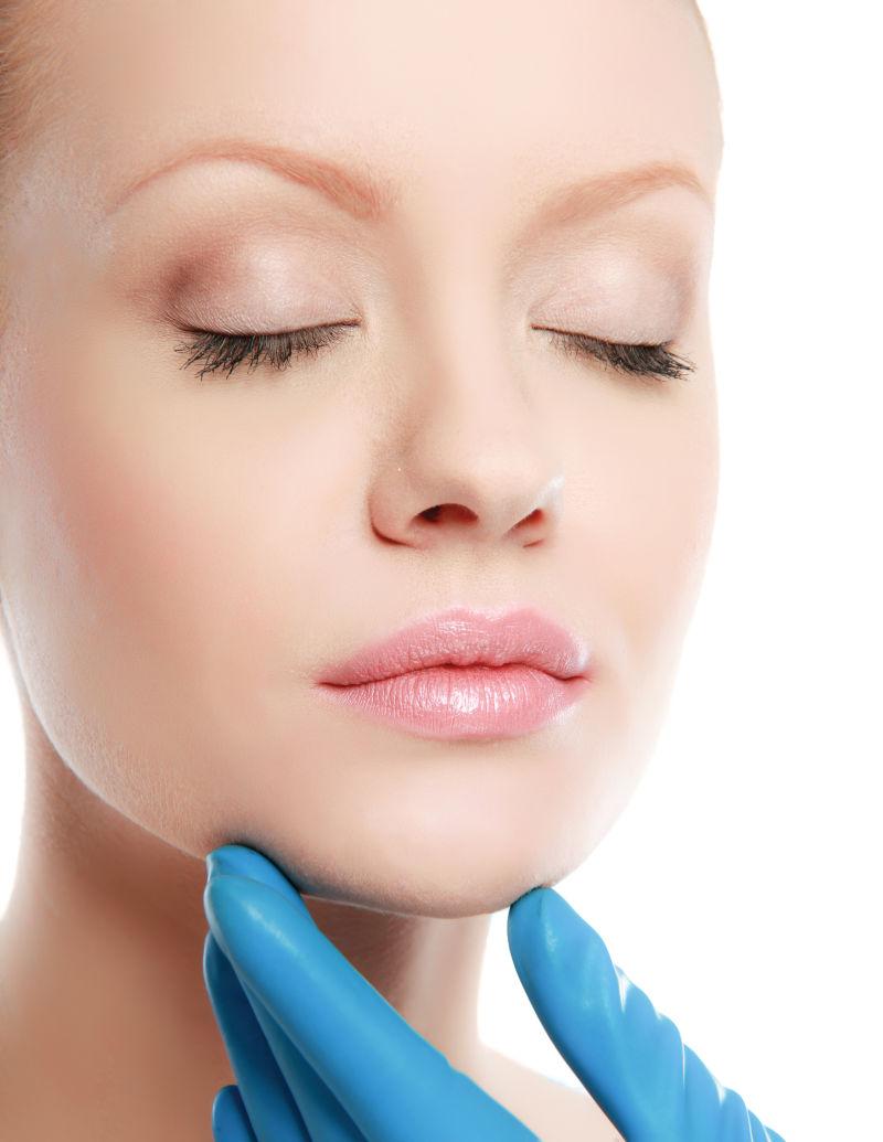 外科医生的手触摸一个漂亮女人的脸