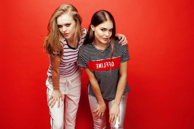 红色背景下两个弓腰的美女