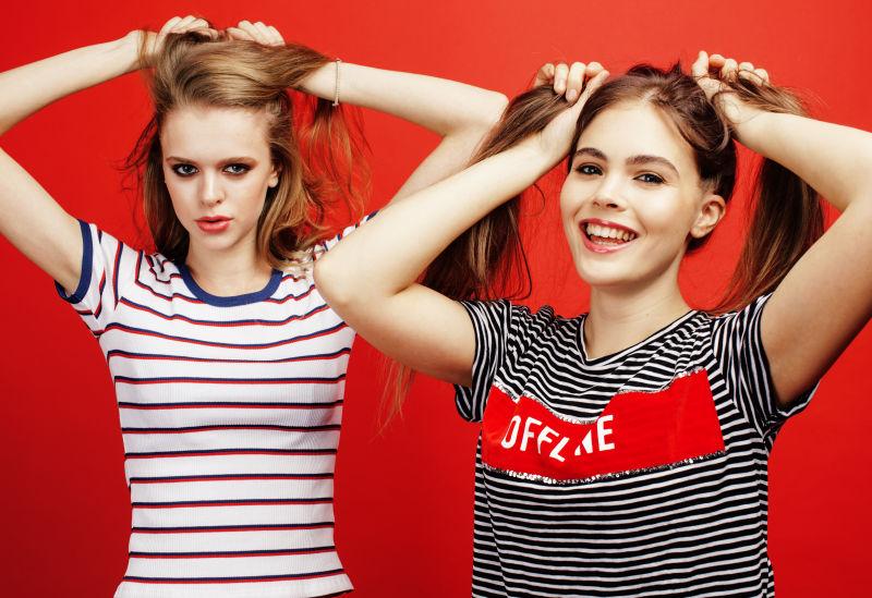 红色背景下两个双手过头顶抓辫子的美女