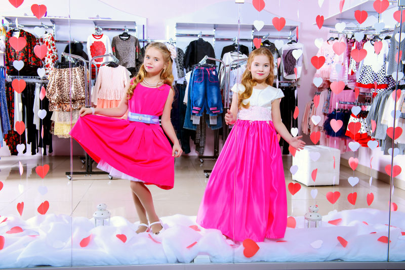 两个可爱的小女孩穿着漂亮的衣服站在儿童服装店的橱窗里